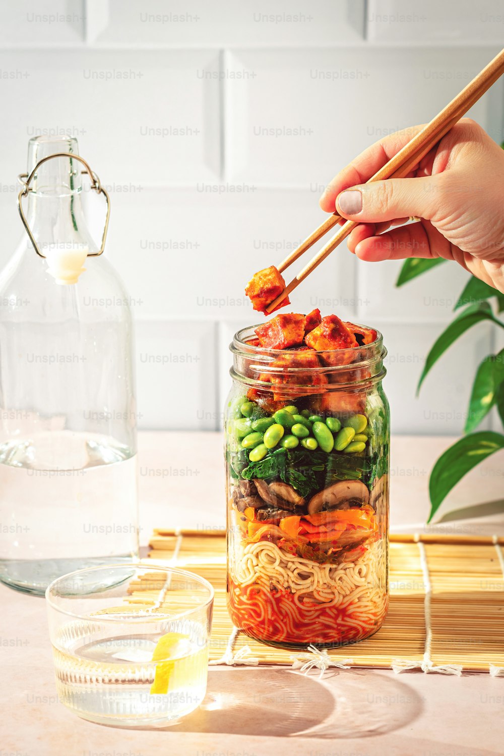 a person holding chopsticks over a jar of food