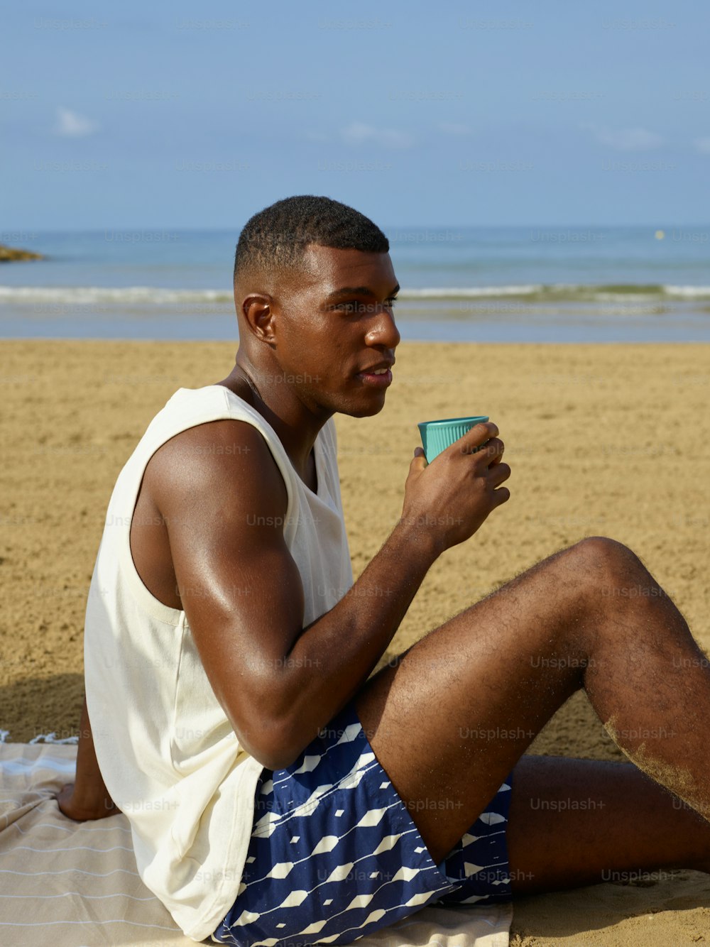 a man sitting on the beach holding a cup of coffee