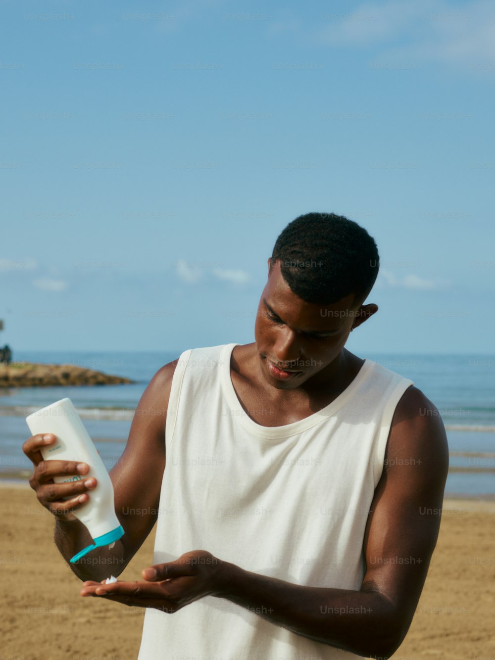 a man standing on a beach holding a bottle