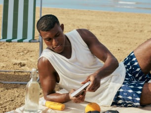 a man sitting on the beach looking at his cell phone