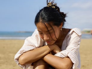 a woman sitting on a beach with her arms crossed