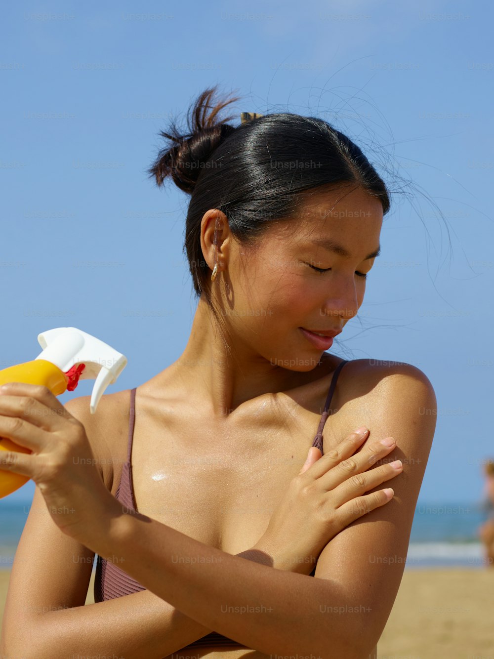 a woman holding a spray bottle and a bottle of sunscreen