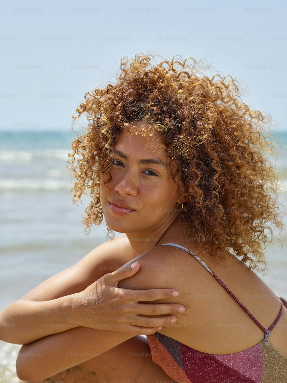 a woman with curly hair sitting on the beach