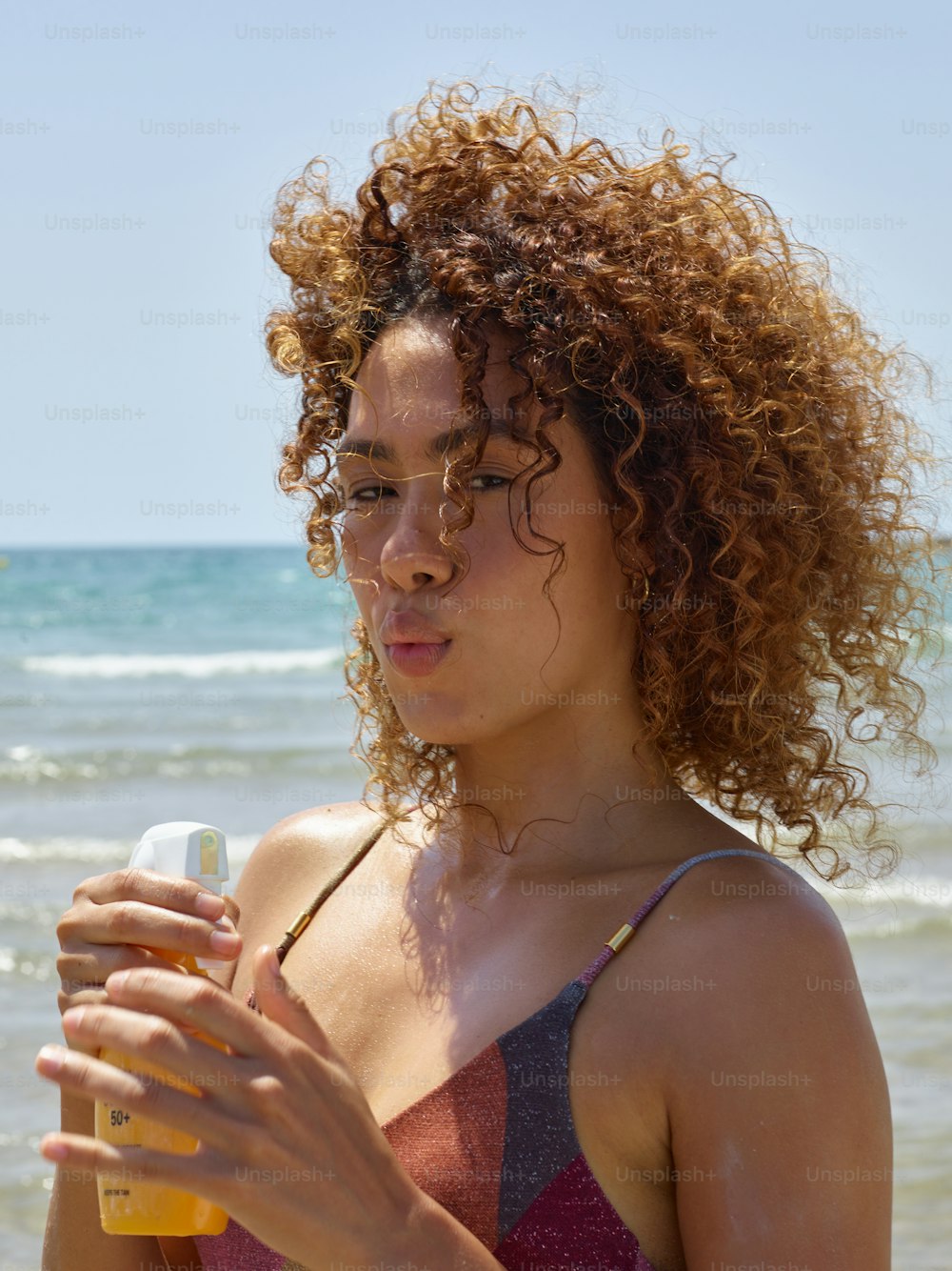 a woman with curly hair holding a bottle of sunscreen