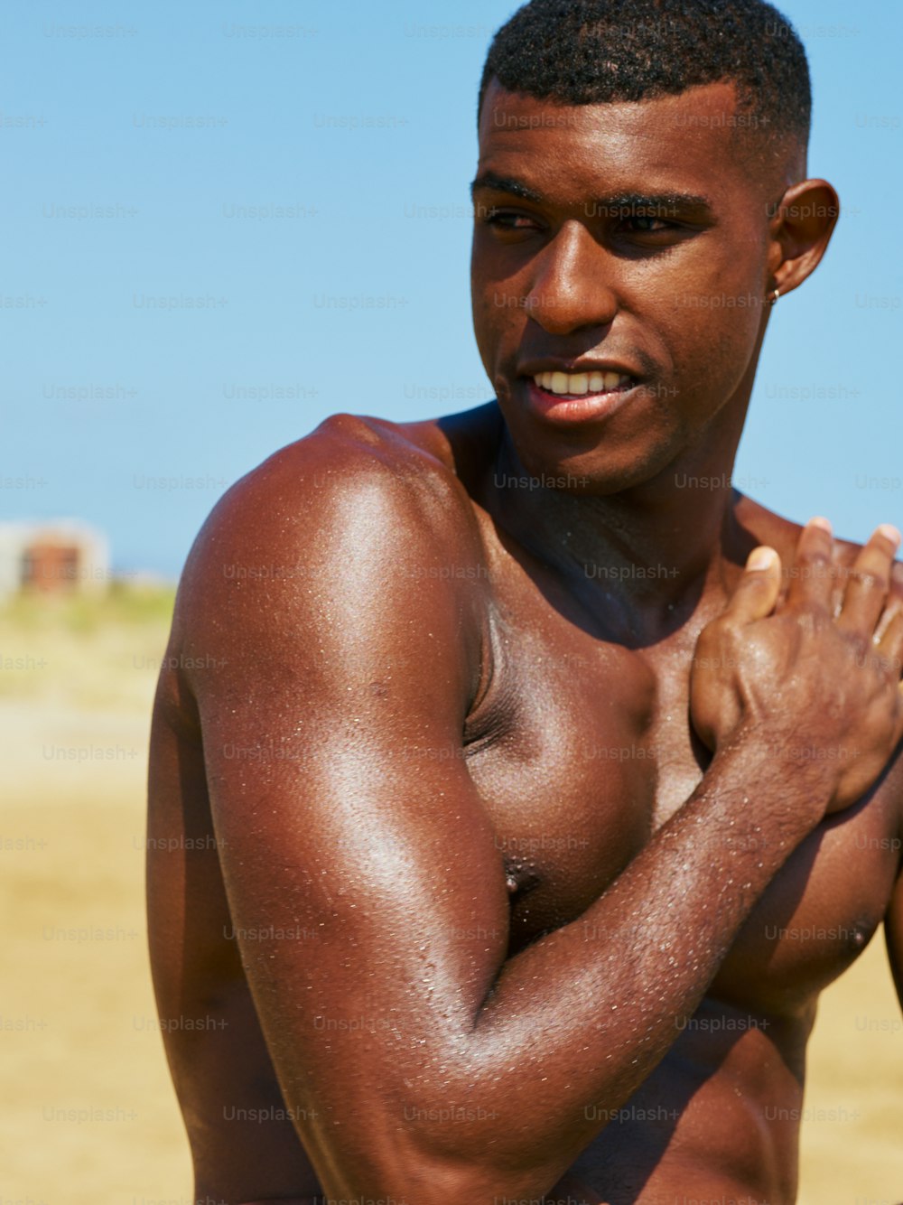 a shirtless man standing on a beach holding his hands together