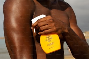 a shirtless man holding a sunscreen on the beach