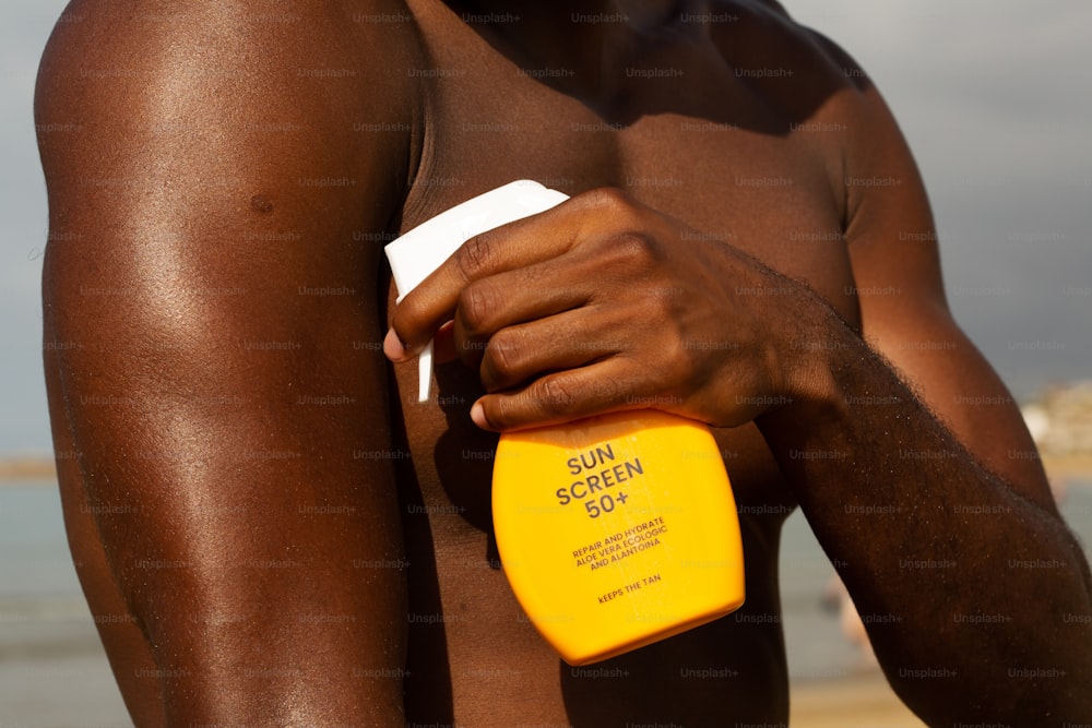 Un hombre sin camisa sosteniendo un protector solar en la playa