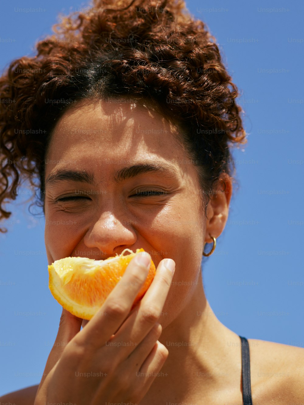 a woman eating an orange slice with a blue sky in the background