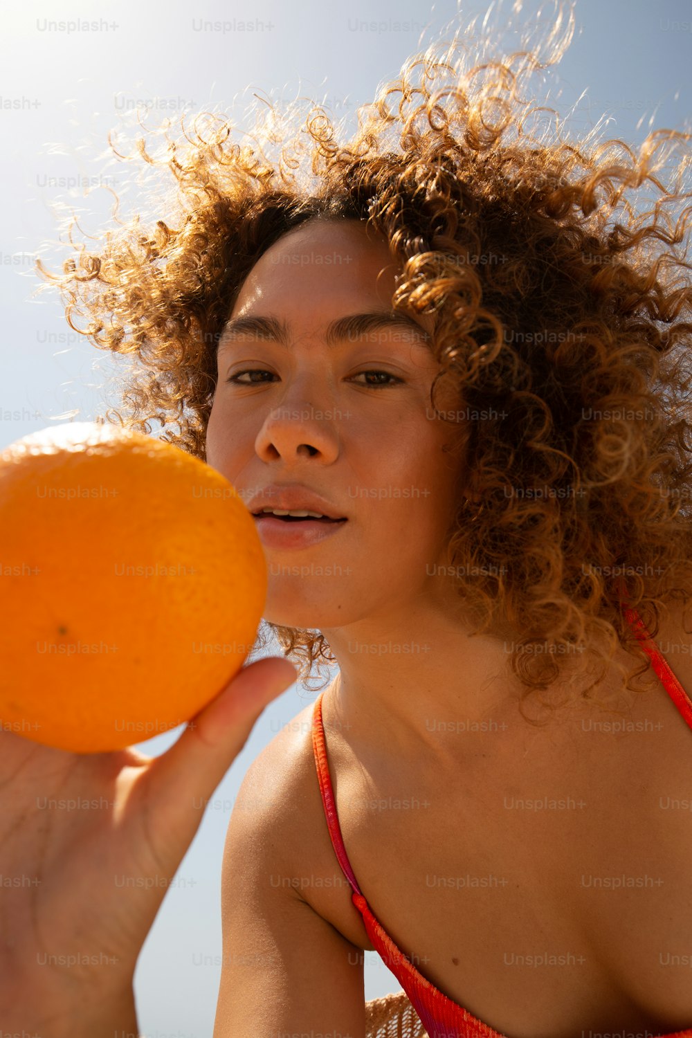 uma mulher de biquíni segurando uma laranja