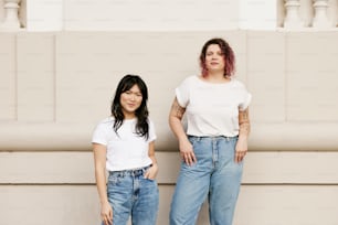 two women standing next to each other in front of a wall