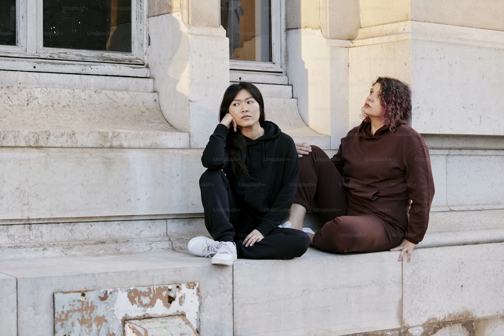 a couple of women sitting on the side of a building