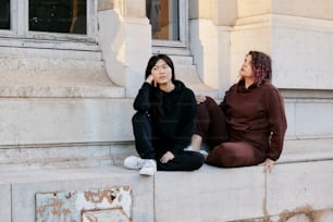 a couple of women sitting on the side of a building