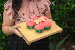 Una mujer sosteniendo una bandeja de cupcakes con glaseado rosa