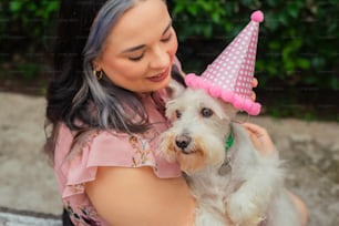 a woman holding a dog wearing a party hat