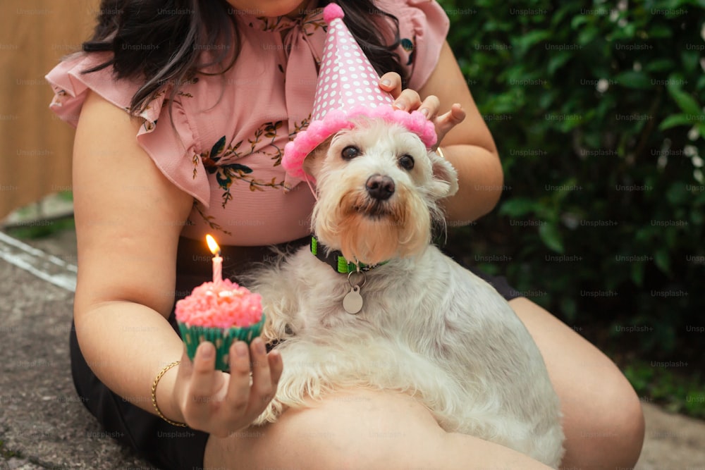 a woman holding a dog and a birthday cupcake