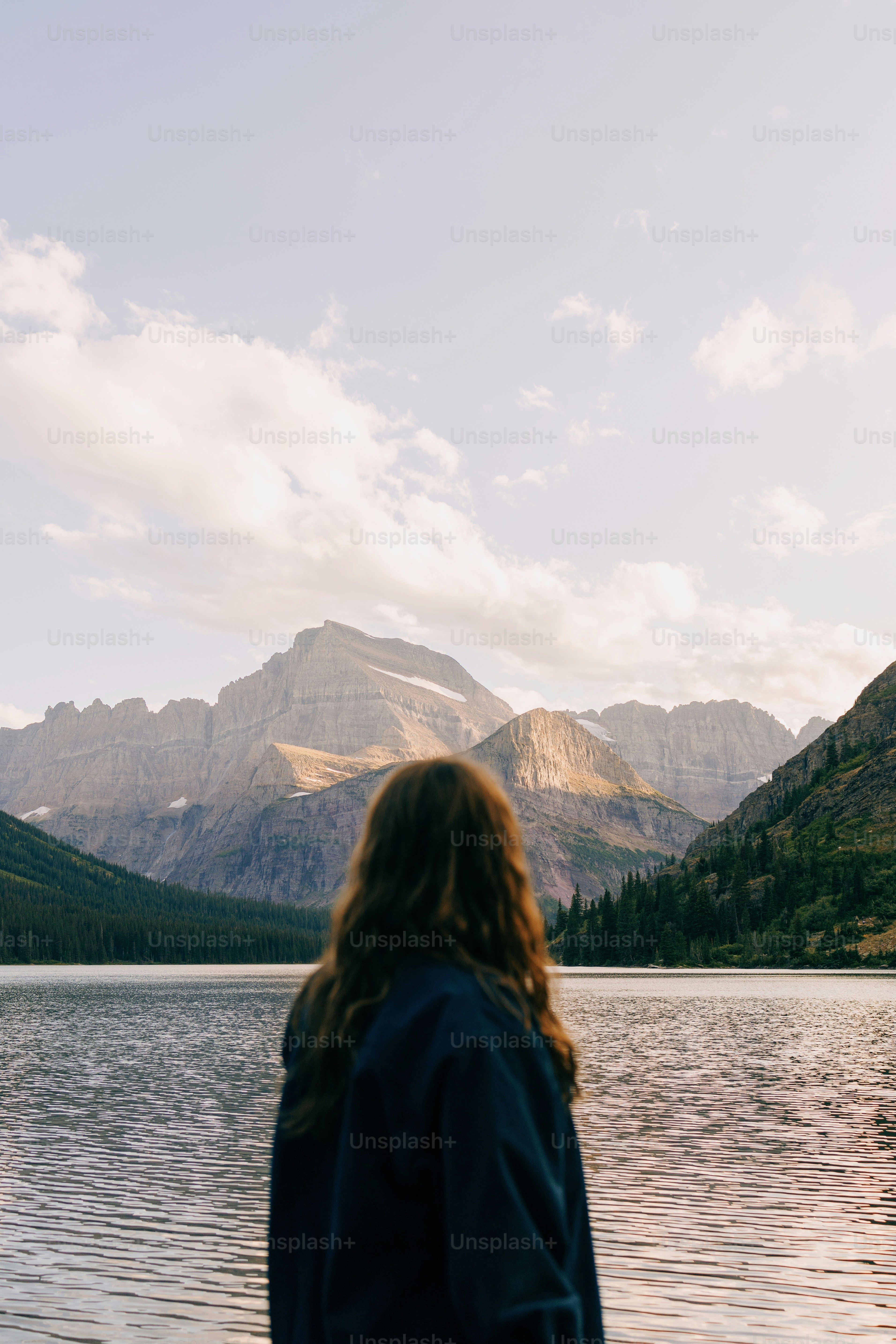 a woman standing in front of a lake with mountains in the background
