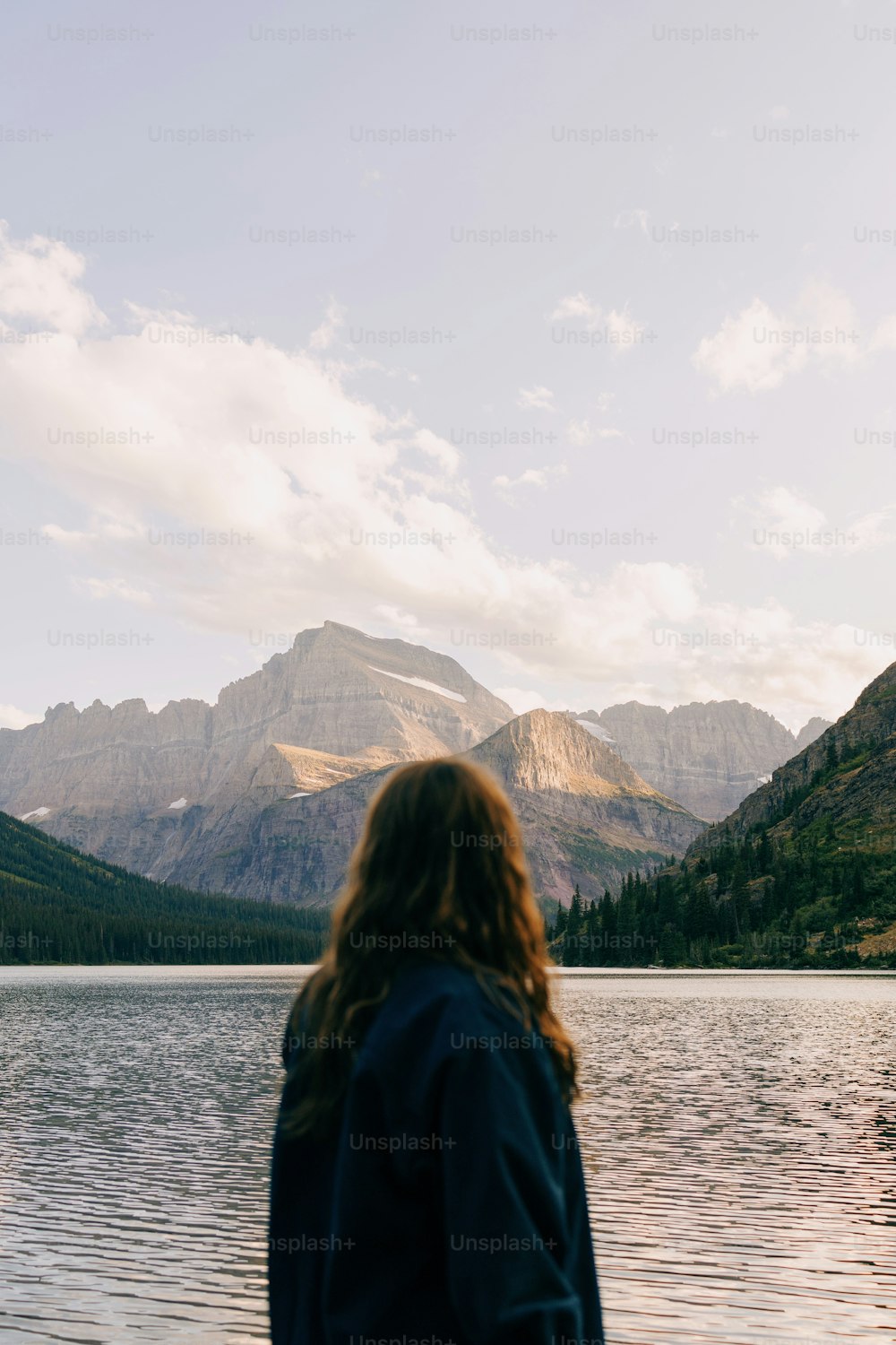 a woman standing in front of a lake with mountains in the background