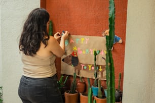 a woman writing on a birthday card next to a cactus