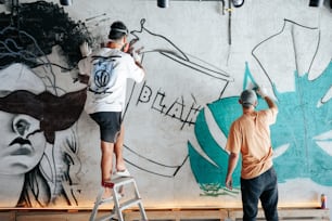 Deux hommes peignent un mur avec des graffitis dessus