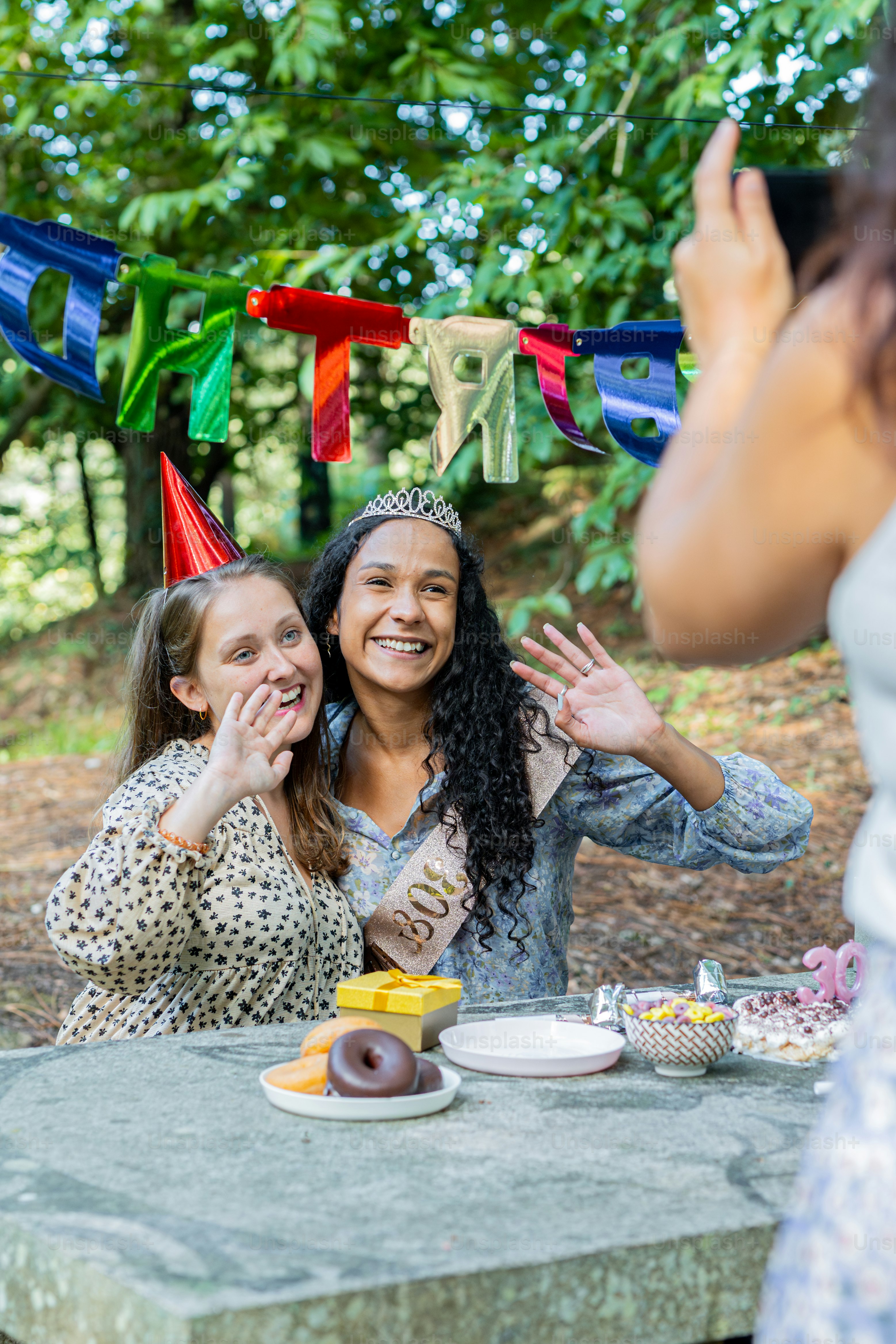 Dos mujeres celebrando un cumpleaños al aire libre con una pancarta.