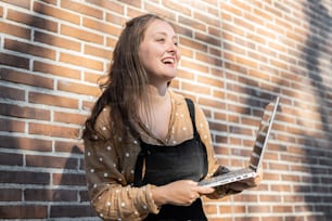 a woman standing in front of a brick wall holding a laptop