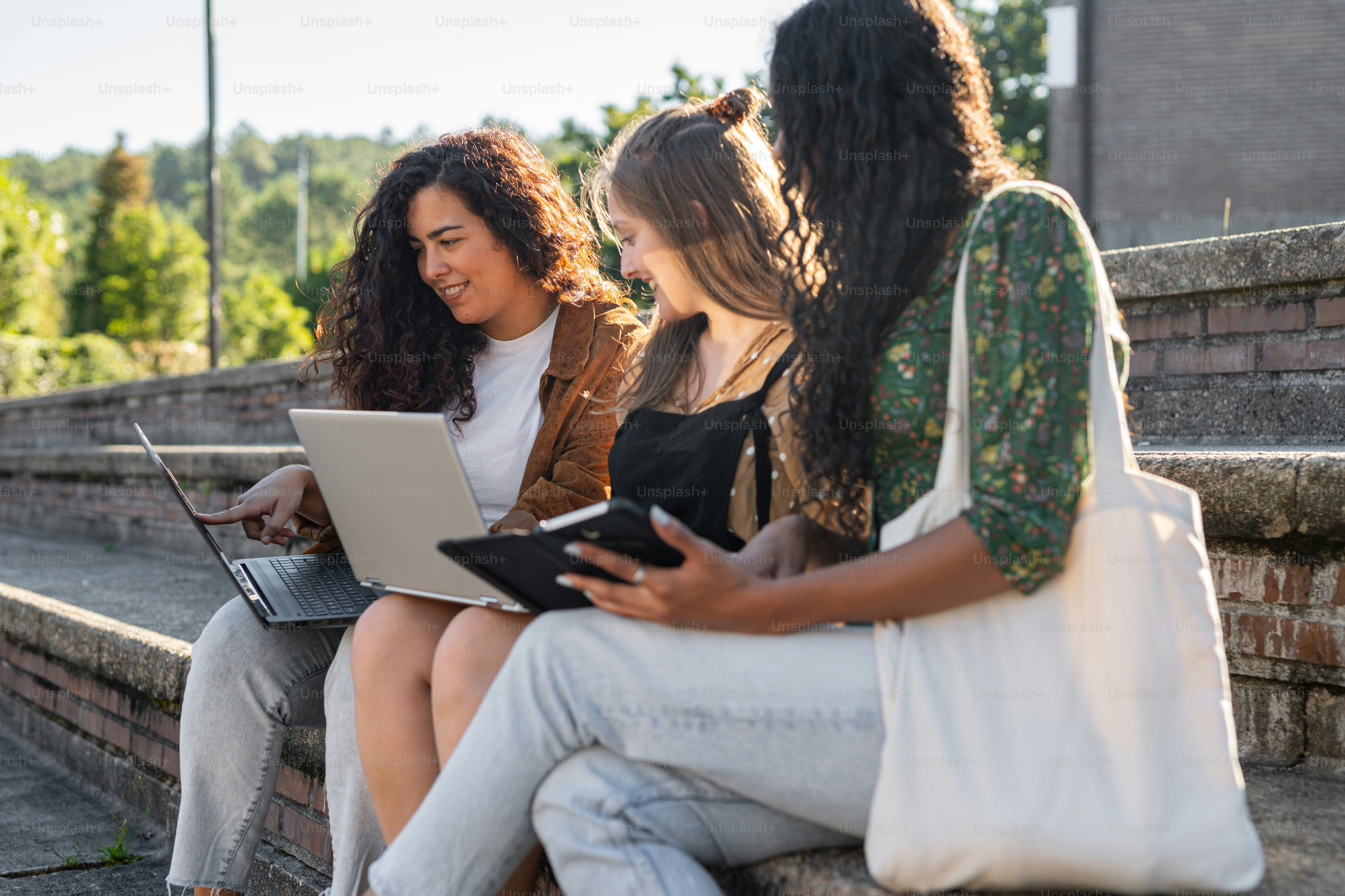 a group of women sitting on the steps with laptops