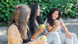 a group of women sitting next to each other holding apples