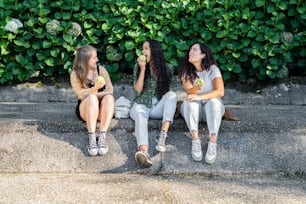 three girls sitting on a curb eating and drinking
