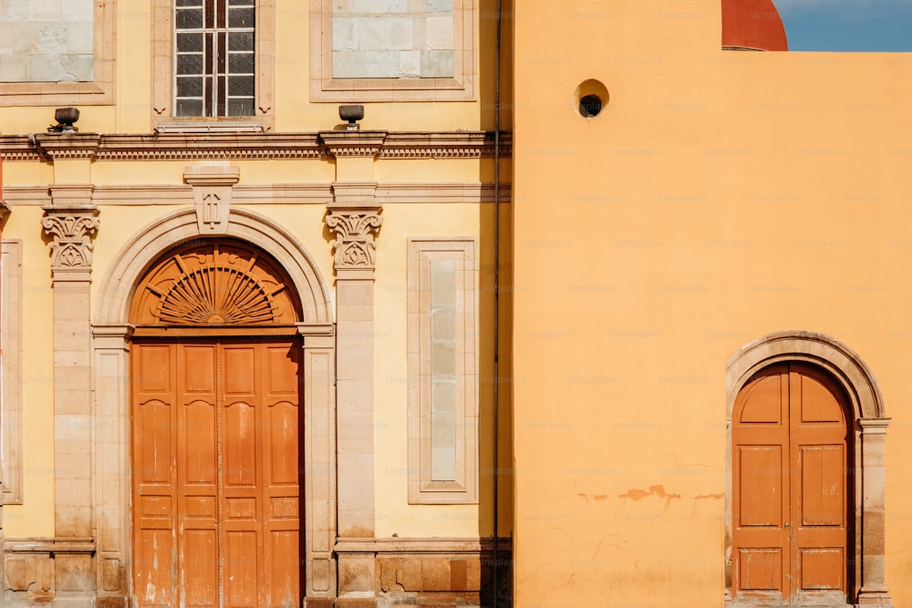 a yellow building with two brown doors and a clock