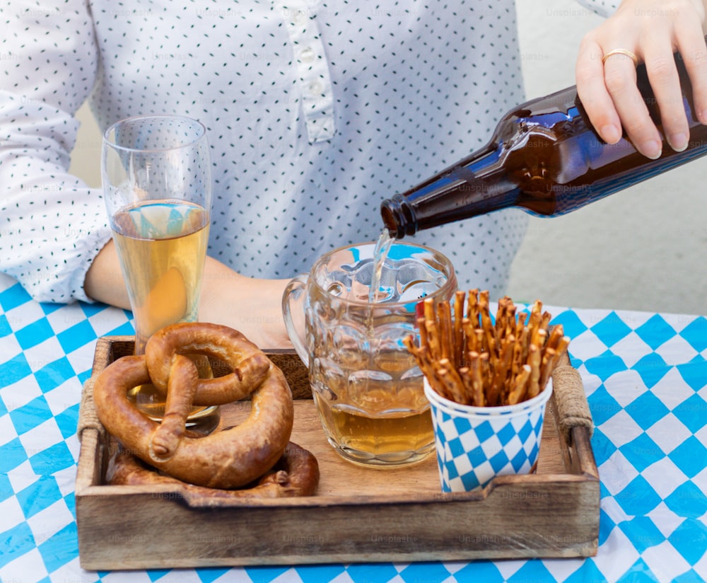 a person pouring beer into a glass next to pretzels and pretzels