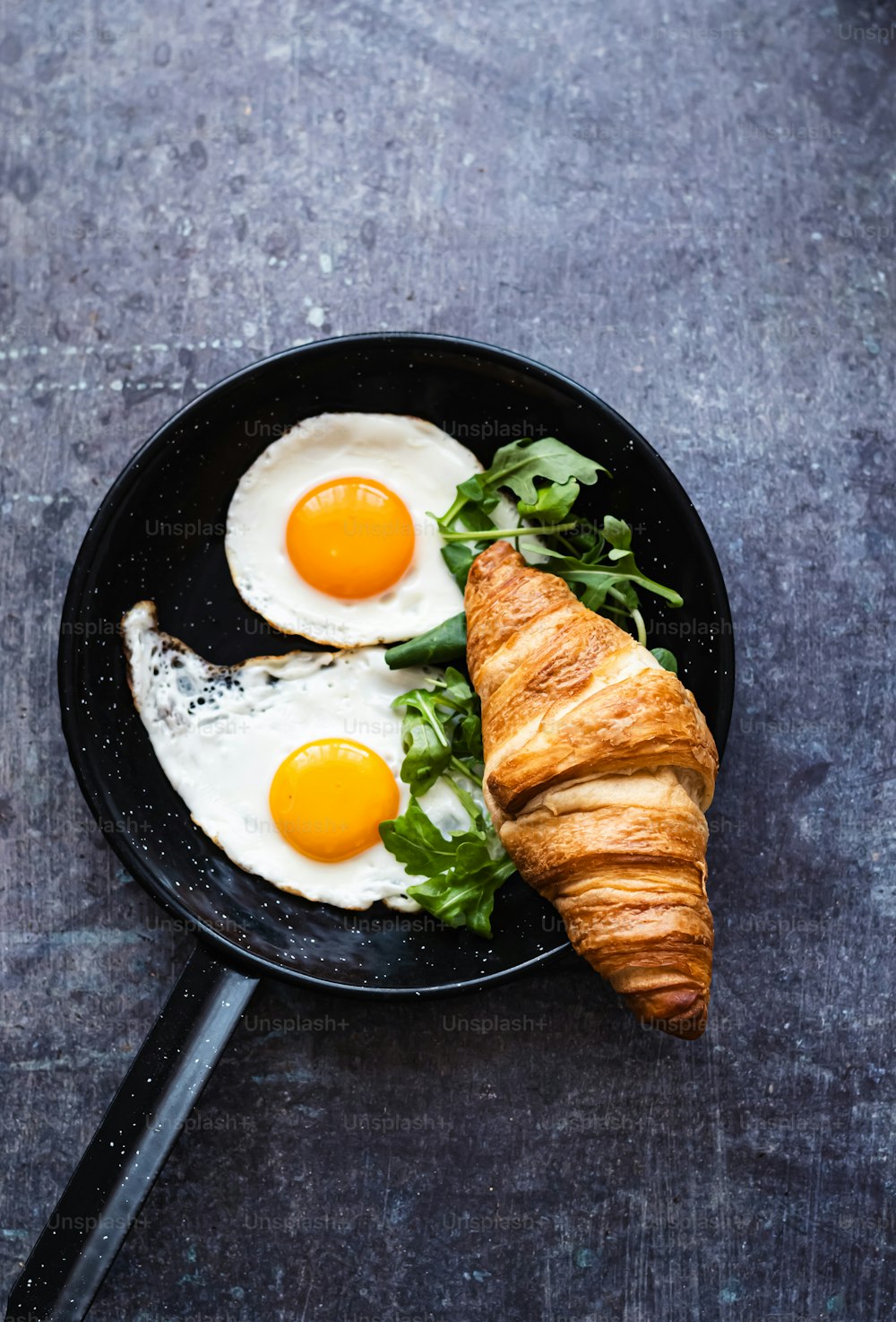 two eggs and croissants in a pan on a table