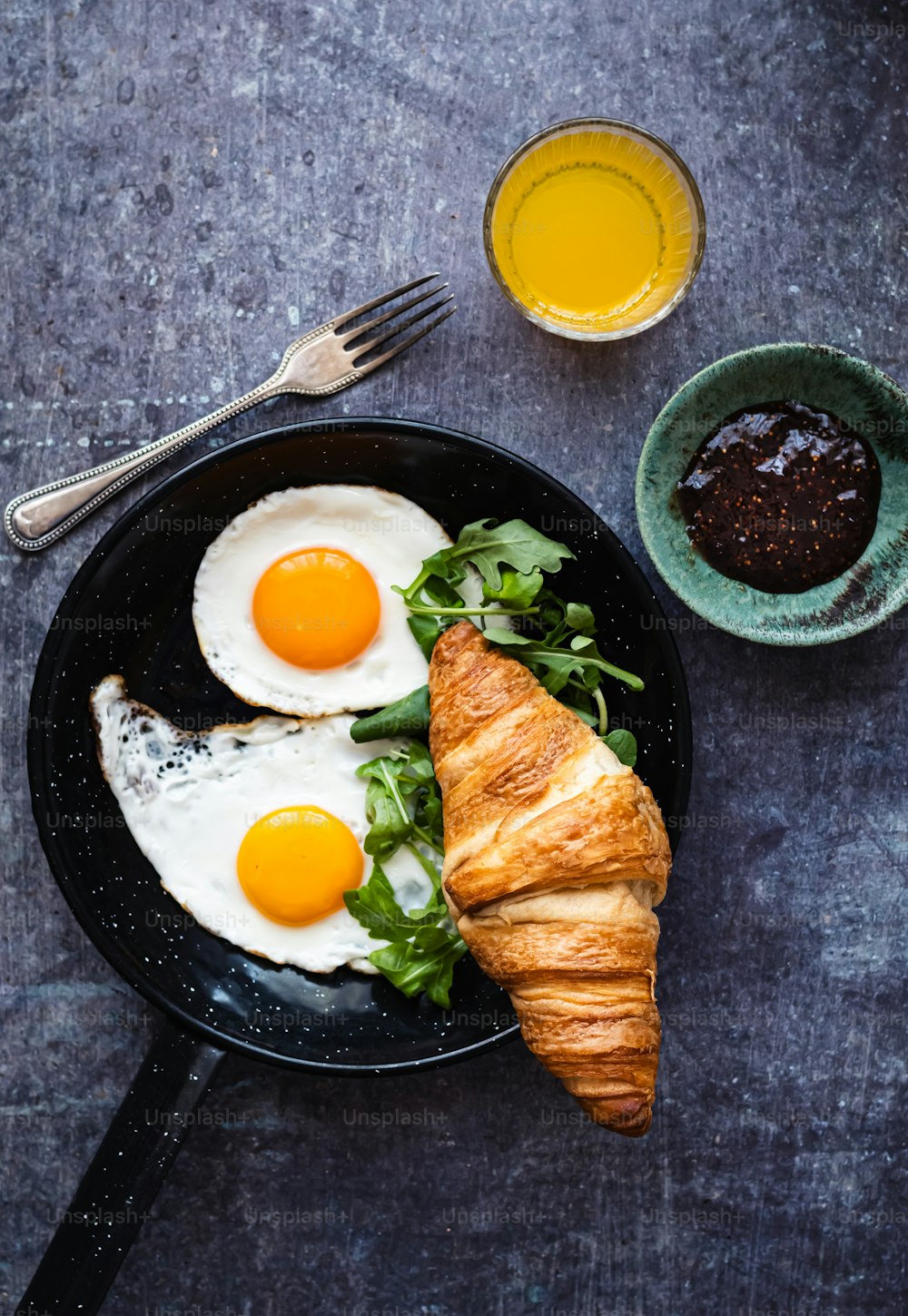 a breakfast of eggs, croissants, and greens on a black plate