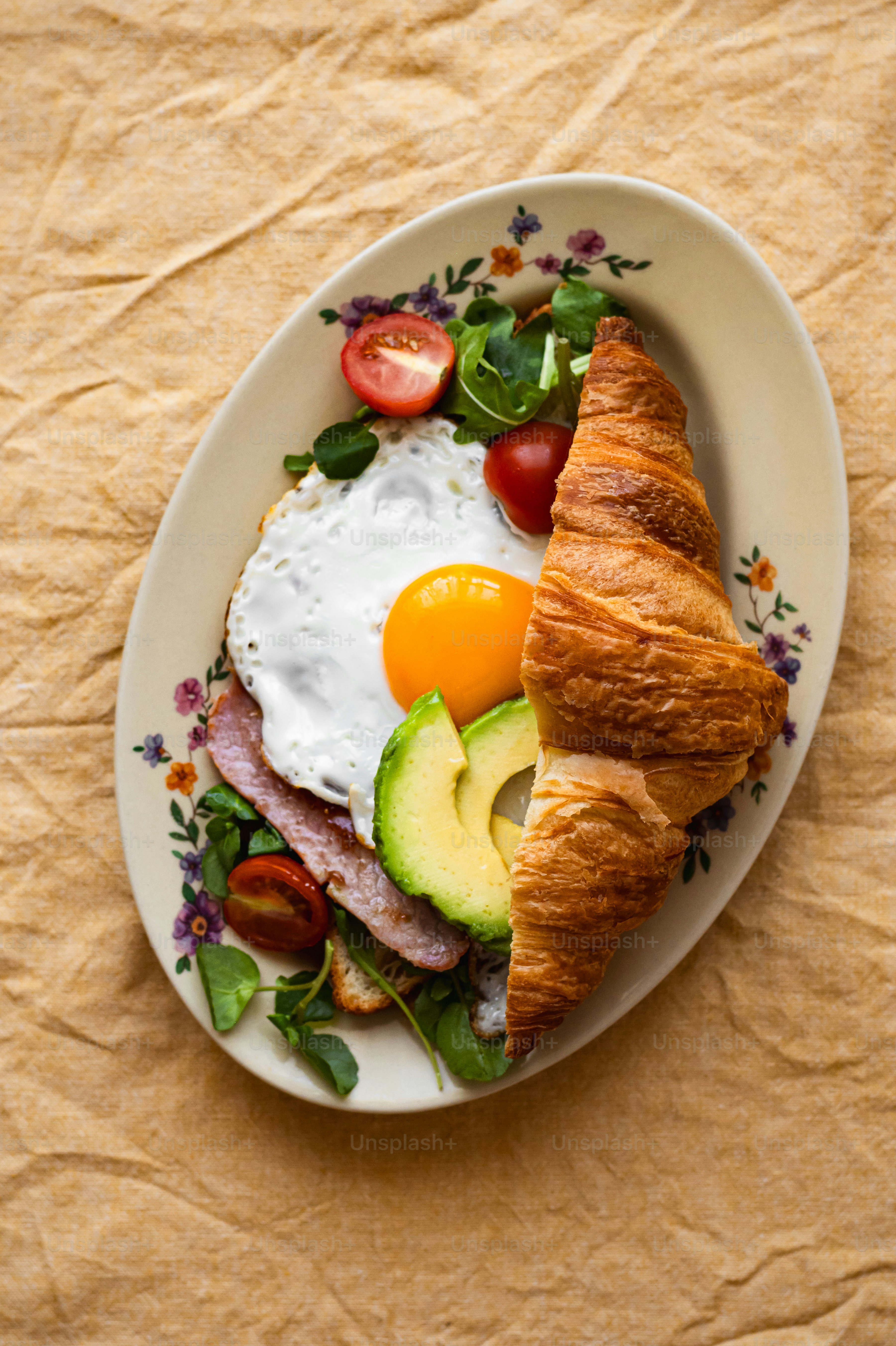 a croissant with an egg, bacon, and avocado on it