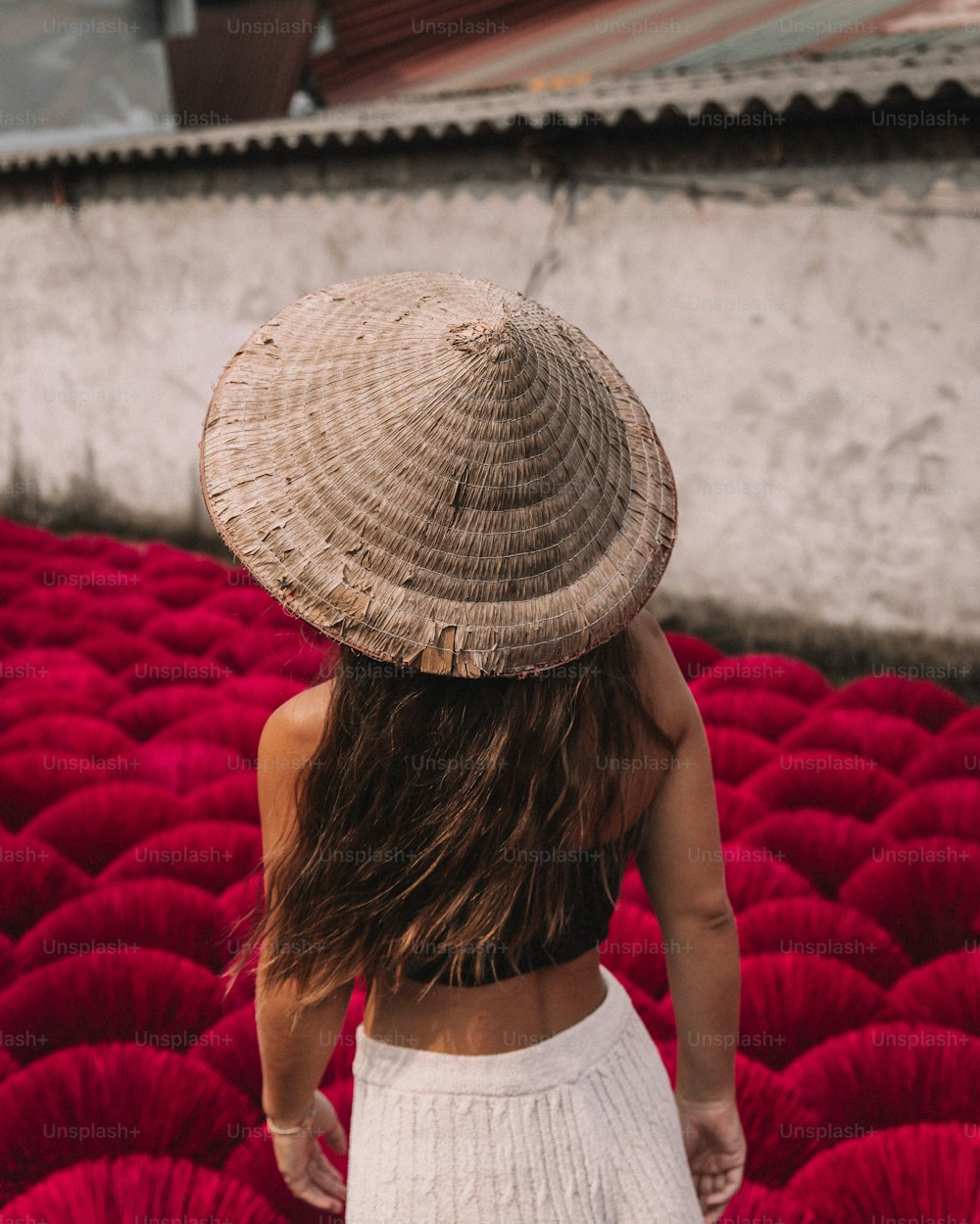 밀짚모자를 쓴 여자가 붉은 꽃밭을 걷고 있다