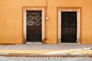 a yellow building with two black doors and a fire hydrant