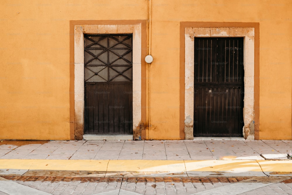 a yellow building with two black doors and a fire hydrant