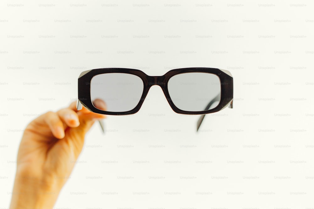 a hand holding up a pair of black glasses