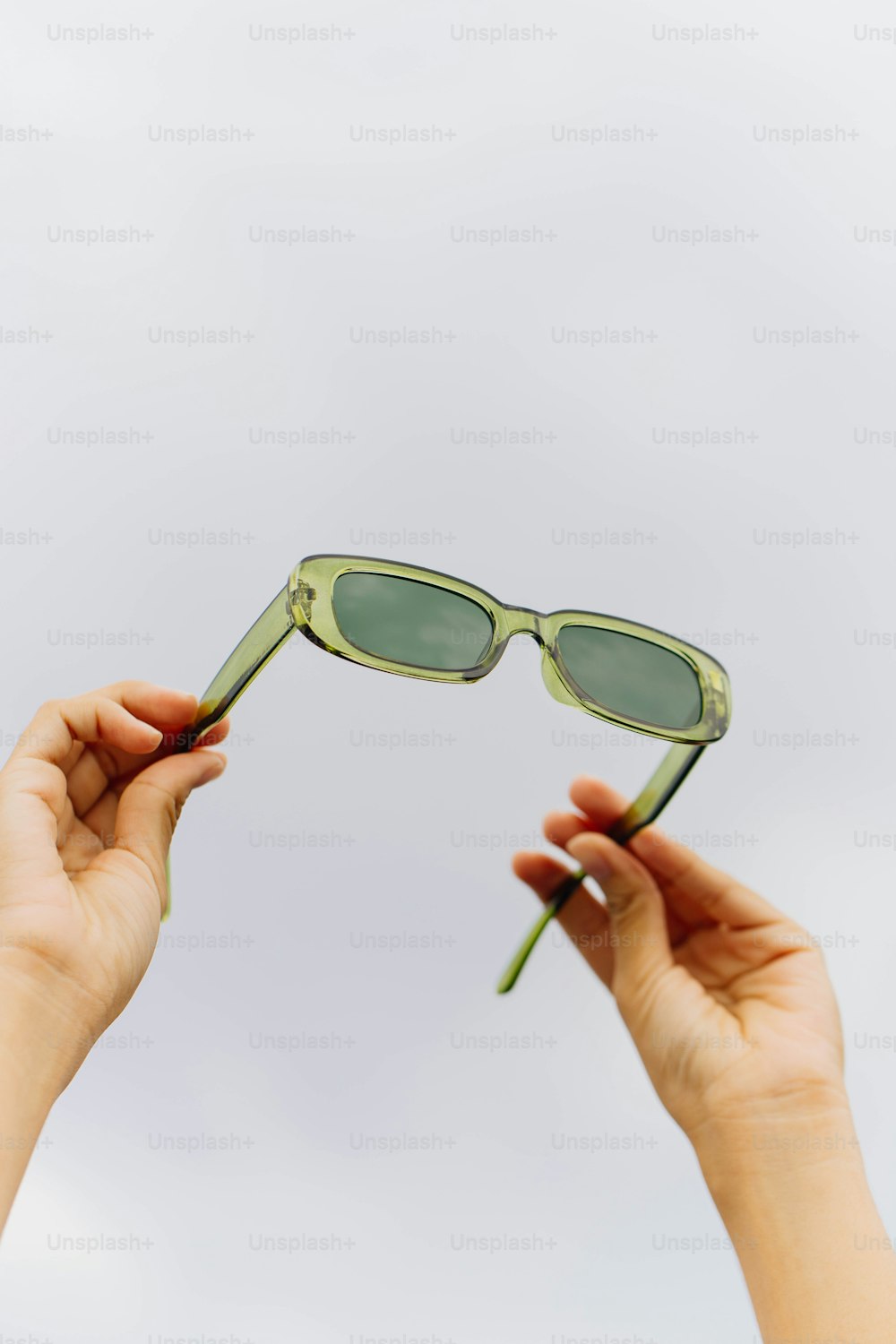a pair of hands holding a pair of green sunglasses