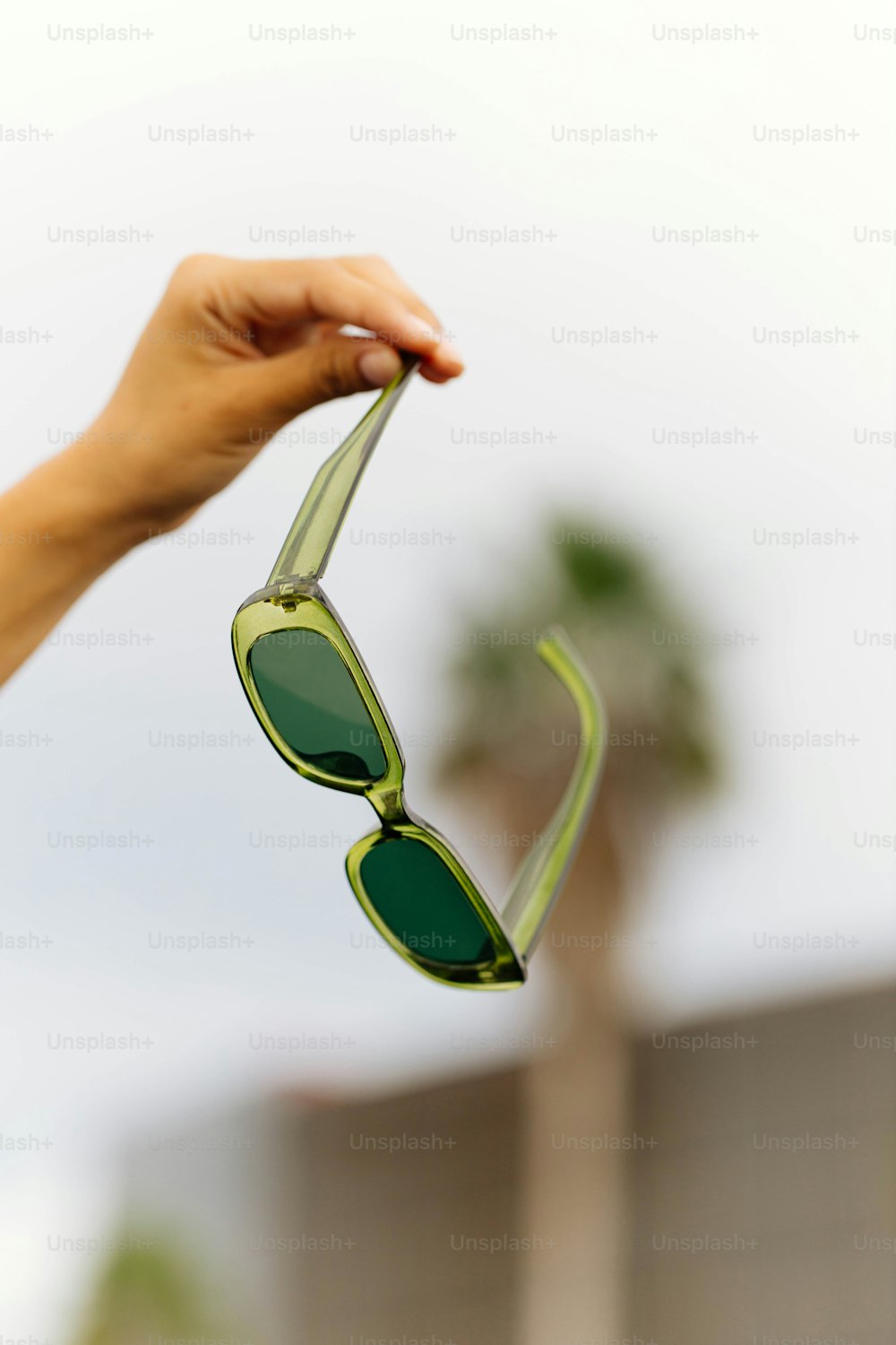 une main tenant une paire de lunettes de soleil vertes