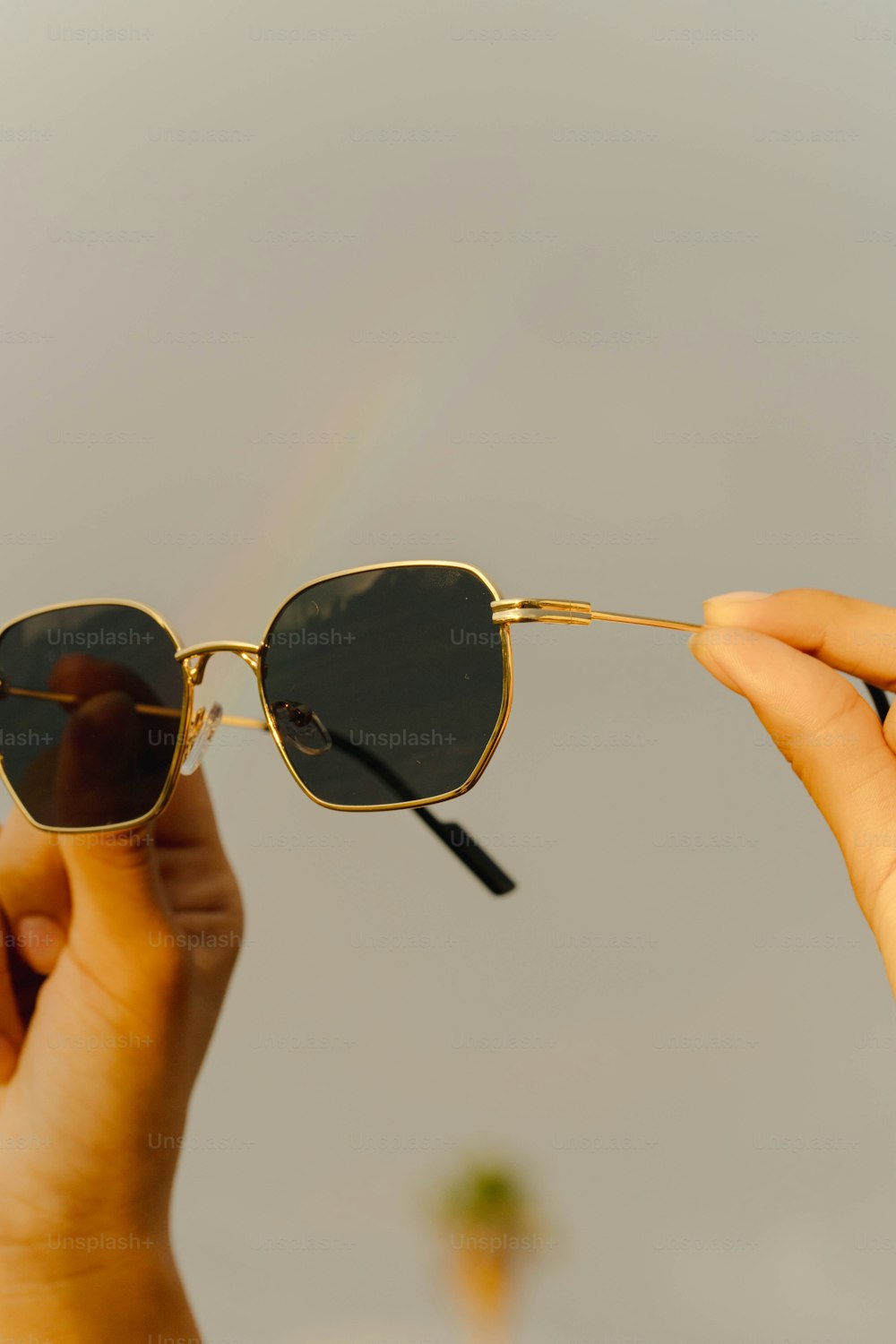 uma pessoa segurando um par de óculos escuros com um arco-íris ao fundo