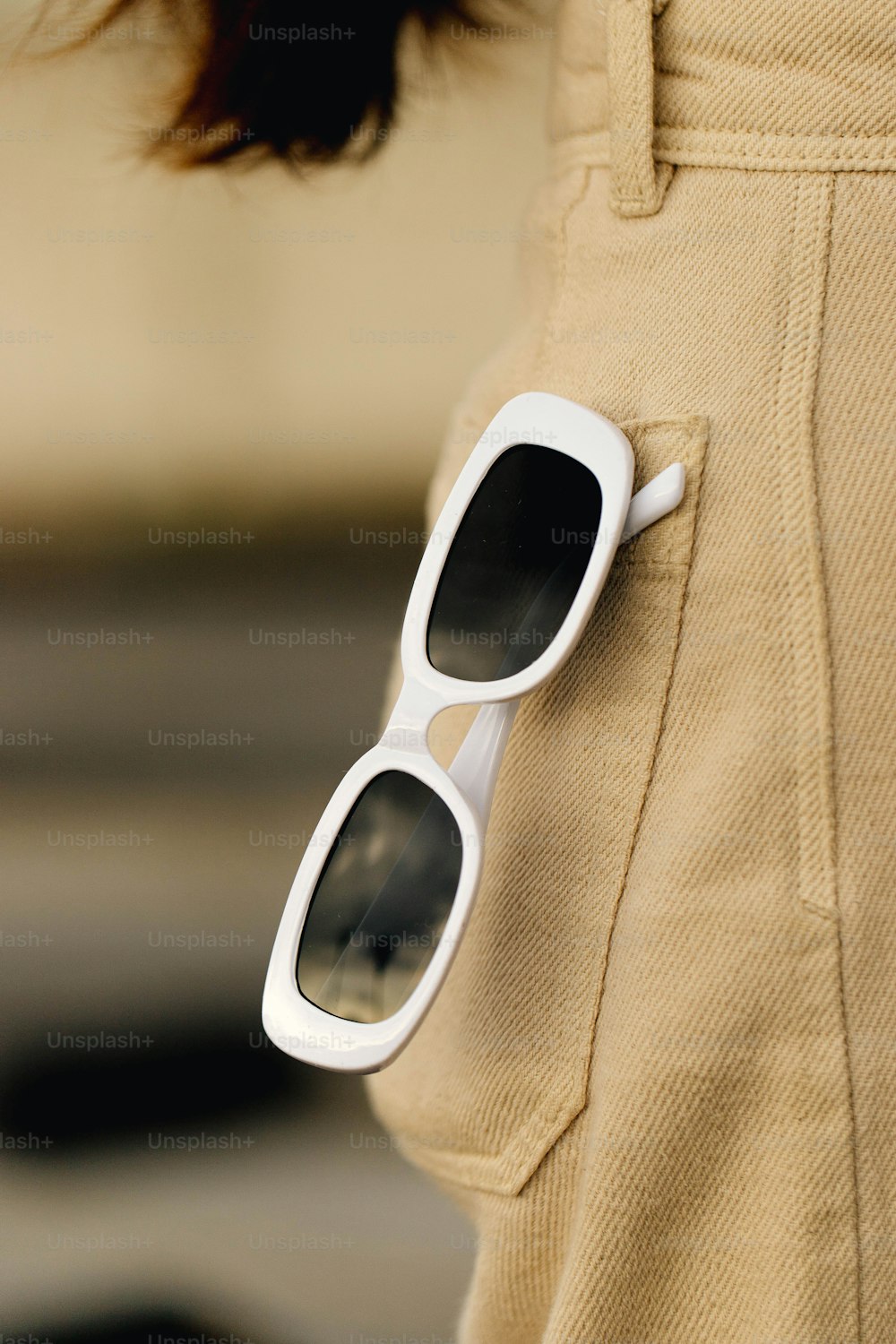a pair of white sunglasses resting on the pocket of a woman's pants