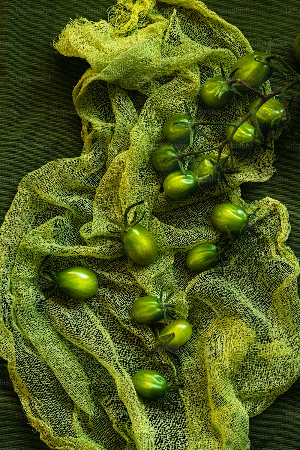 um cacho de tomates verdes sentados em cima de um pano verde