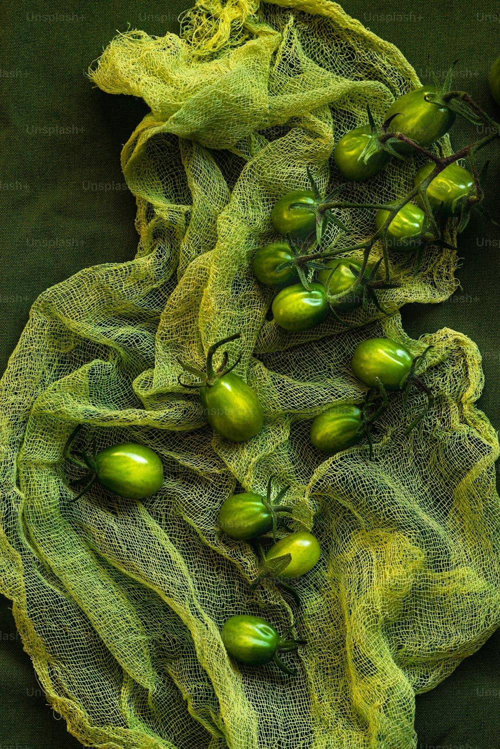 a bunch of green tomatoes sitting on top of a green cloth