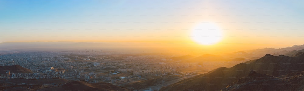 the sun is setting over a city in the mountains