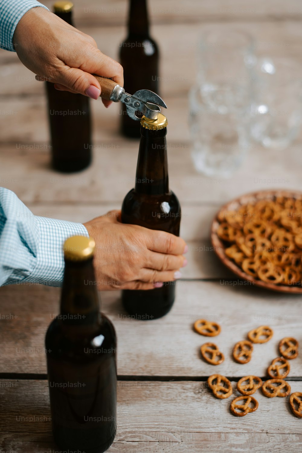 a person opening a bottle of beer with pretzels on the table