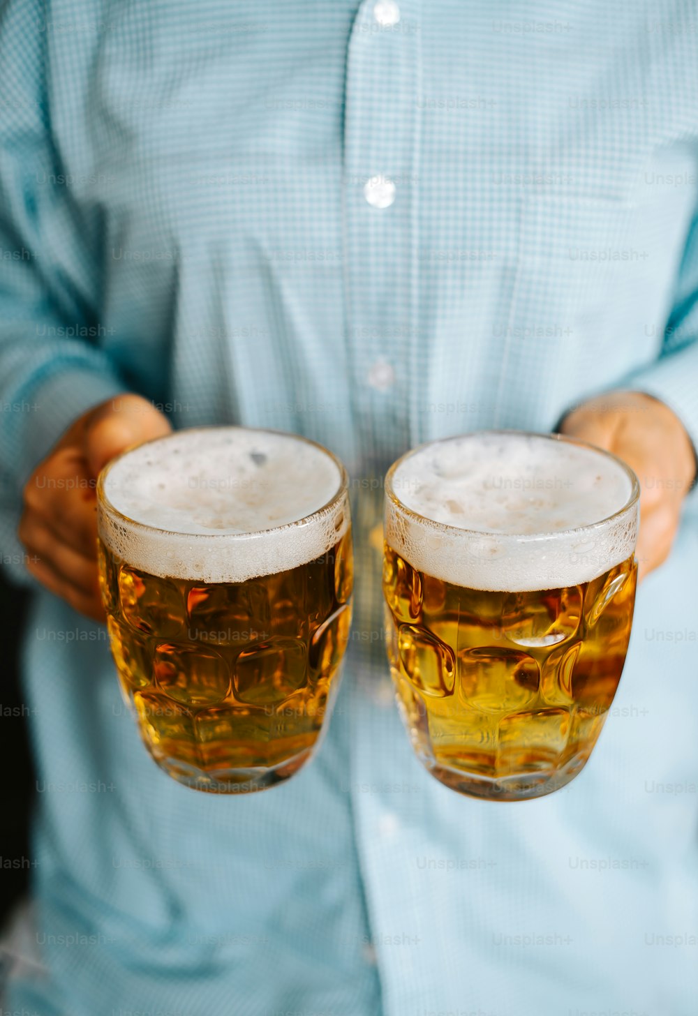 a man holding two glasses of beer in his hands