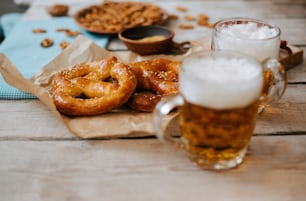 a wooden table topped with two mugs of beer and pretzels