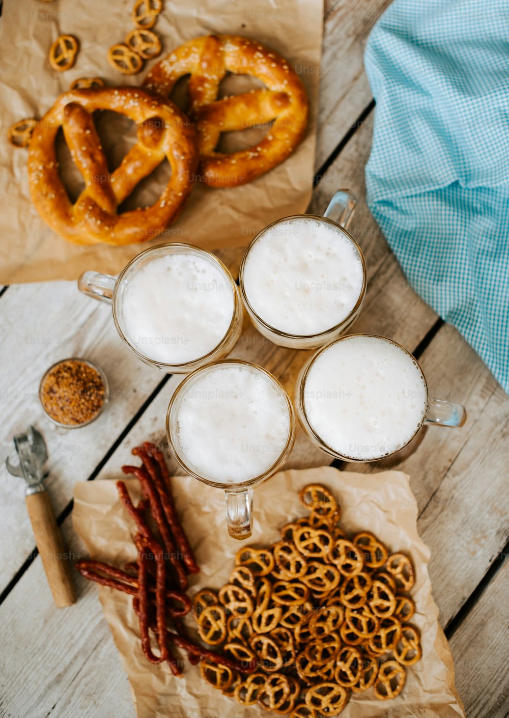 a wooden table topped with two mugs of beer and pretzels