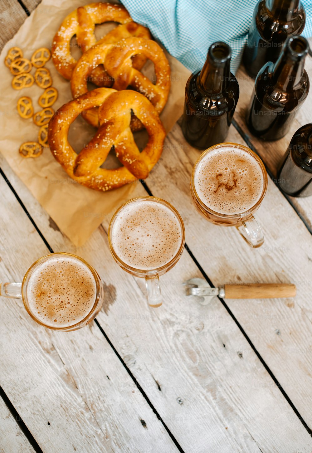 a wooden table topped with glasses of beer and pretzels