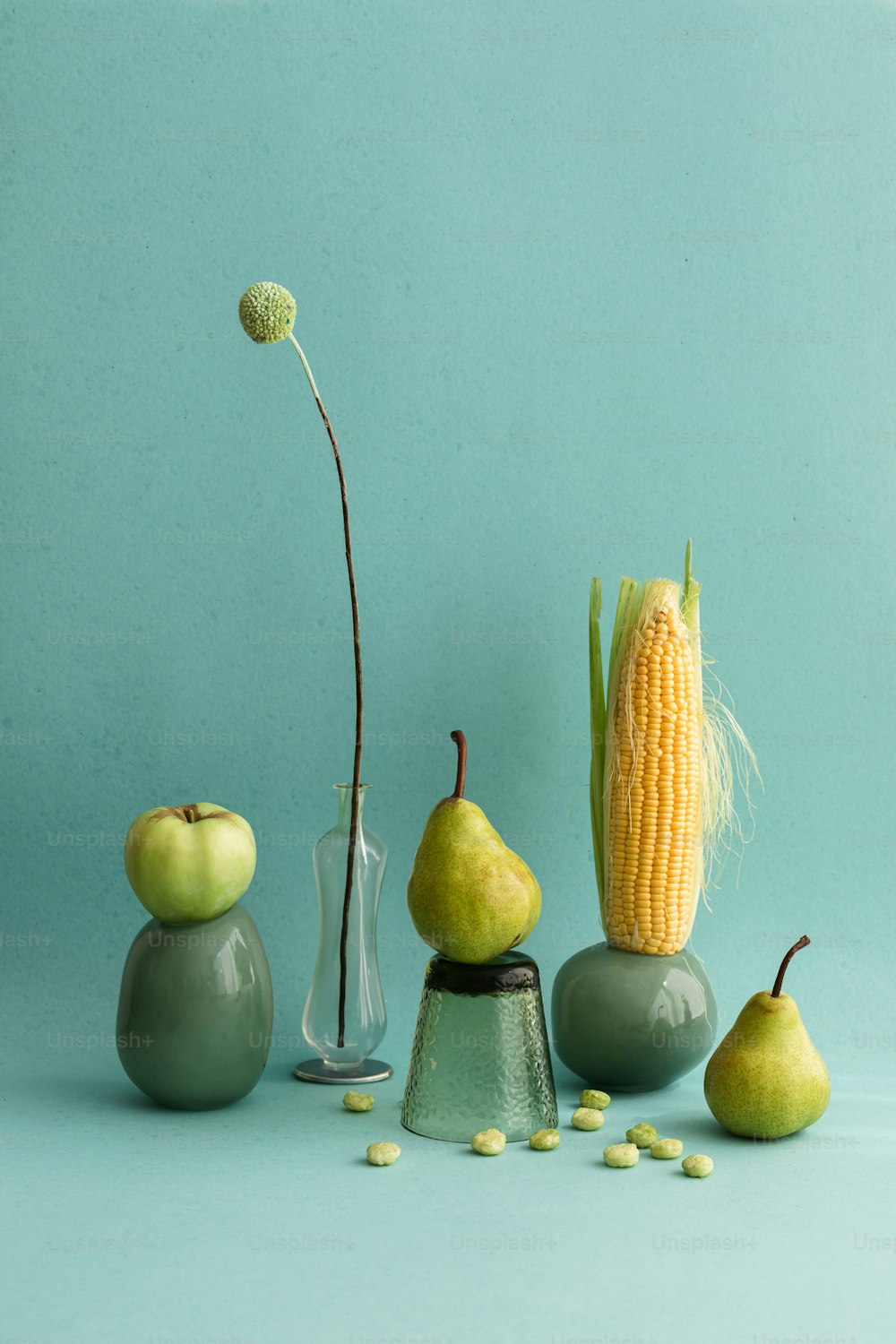 a corn on the cob, a vase, and two pears on a